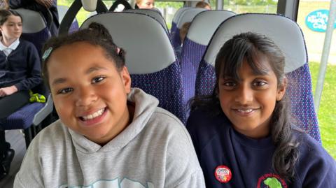 Two girls smile at the camera as they ride on the bus as part of a promotional event for Kids Go Free.