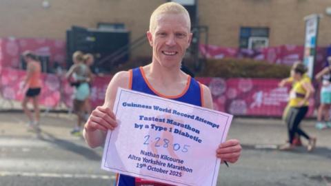 Image of Nathan in his running vest. He is holding up a sig which reads: GUINESS WORLD RECORD ATTEMPT FASTEST MARATHON BY A TYPE 1 DIABETIC: 2:28:05 NATHAN KILCOURSE ALTRA YORKSHIRE MARATHON 19TH OCTOBER 2025