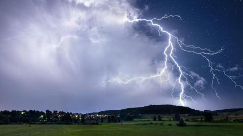 Lightning flashes across the night sky and strikes farmland.