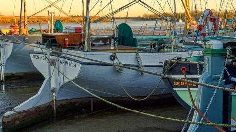 There are a number of boats moored. The background weather is clear and looks like it could be a sunrise or a sunset.