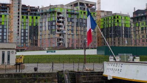 An apartment block covered in scaffolding and building materials. It is situated beside the SS Nomadic boat at the Titanic slipway. 