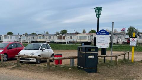 View of the sparsely populated North Beach car park at Heacham. There are three cars parked on the sand next to a parking metre and a yellow barrier limiting the height of cars that can be parked there.