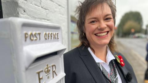 On the left, a picture of a white postbox with gold letters affixed to a wall and on the right, a grinning woman with nose and lip rings looking at the camera