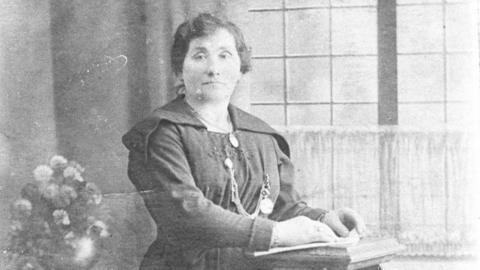 A black and white photo of a woman. She looks to be middle-aged and wears a dark dress - as she poses for a 19th century photograph.