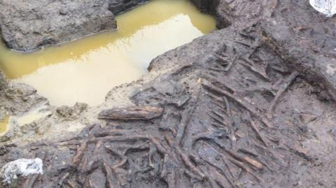 Brown pool of water, which sits next to a muddy bank, where a wooden structure is exposed.