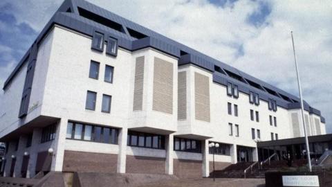 An exterior view of Maidstone Crown Court - a big white building with multiple windows with a modern grey roof. Steps lead up to the court entrance.