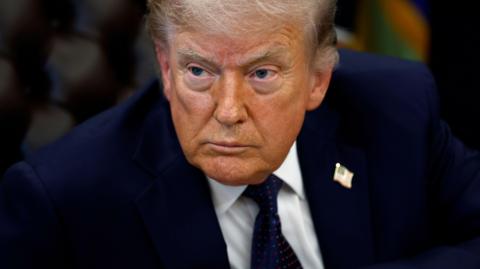 Close up of Donald Trump looking intensely to his right while sitting down at his desk in the Oval Office