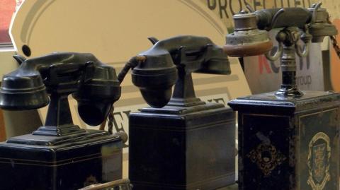 Three telephones from the early 20th century. Two are coloured black and have handsets resting on top of tall, rectangular boxes. The third has a metallic handset resting on a black box with an ornate crest of arms featuring the three crowns of the Hull council.