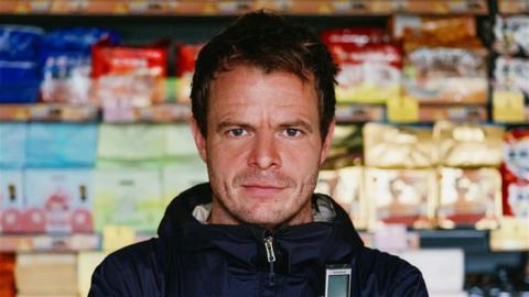 Dan Kelly stands in front of a shelf of products.
