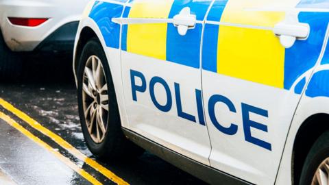 Stock imagine of a blue and yellow police car, pictured from the door handles down