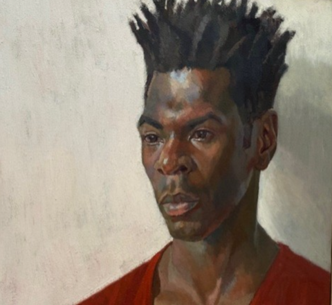 A head and shoulders portrait of the artist Nahem Shoa shows him wearing a plain red top, looking slightly off to the right, his gaze fixed on somthing or somone we can't see.