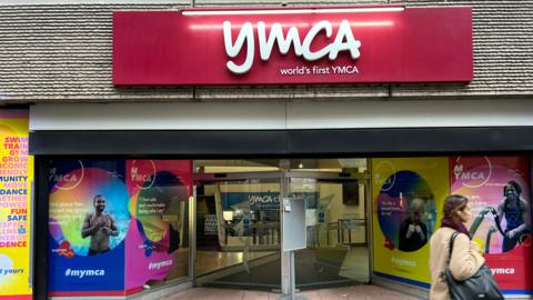 A woman walks past Central London's YMCA which has a red sign with white letters spelling 'YMCA, world's first YMCA'