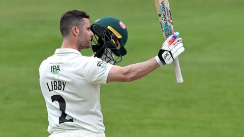 Jake Libby holds bat and helmet aloft 