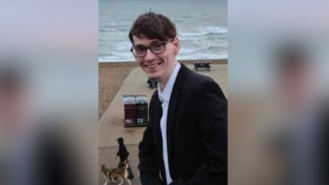A young man in glasses and a suit on a beach