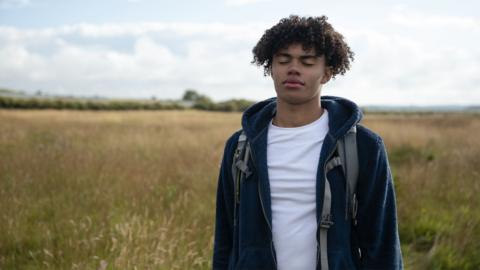 Teenager standing in nature with his eyes closed looking calm.