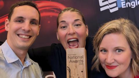 Three members of the swimming academy smiling with a wooden trophy between them