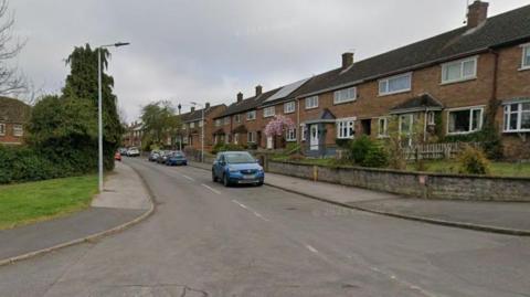 Road with houses on both sides. There are a few cars.