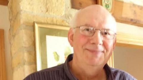 David Hill, who has white hair and glasses smiling straight at the camera.