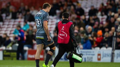 Max Llewellyn (left) walks off the pitch with a medic beside him