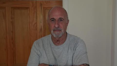 Richard Manville stands with his arms crossed wearing a grey t-shirt