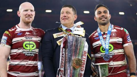 Matt Peet, in the middle of the picture, head coach of Wigan Warriors, lifts the Super League Trophy, alongside Liam Farrell on the left and Bevan French on the right after his team's victory in the Betfred Super League Grand Final between Wigan Warriors and Hull Kingston Rovers