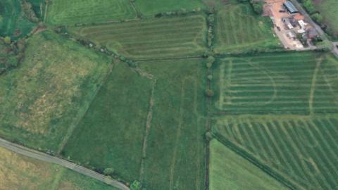 A satellite shot shows fields, separated by hedgerows, with a road at the bottom left and farm buildings at the top right.
