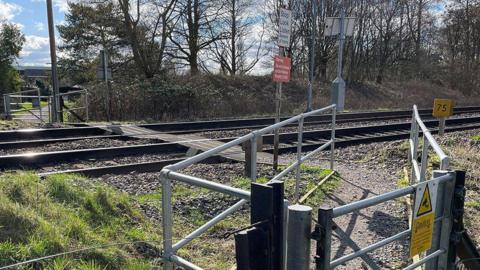 The train line at Pewsey footpath crossing. There are metal gates either side of the train track with caution signs and signage instructing pedestrians to stop look and listen.