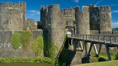 A general view of Caerphilly castle with a moat in the foreground, and a bridge across it.