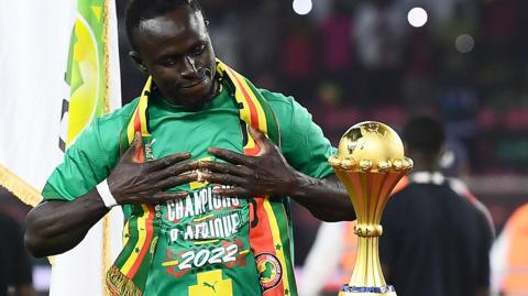 Sadio Mane holds his hands to his chest as he admires the Africa Cup of Nations trophy, which stands on a plinth