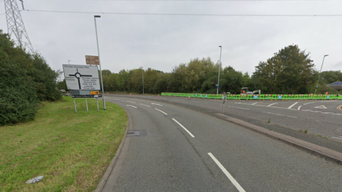 A looping slip road with a road sign for the coming roundabout