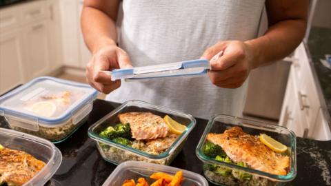 Man wearing a white shirt places plastic lid on top of glass food container