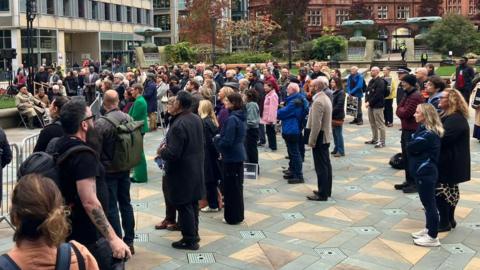 A crowd of people face a stage in a city centre location.