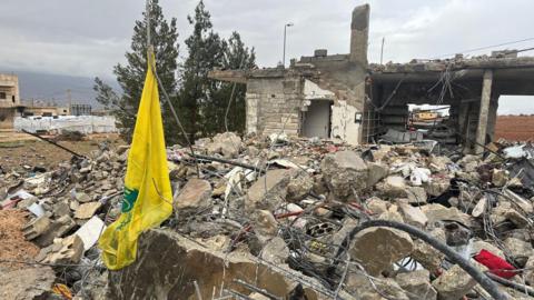 The yellow flag of the Hezbollah group hanging by the ruins of a house