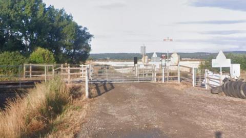 A railway crossing on a rural dirt road near Worlaby, North Lincolnshire. The white gates of the crossing block the road.