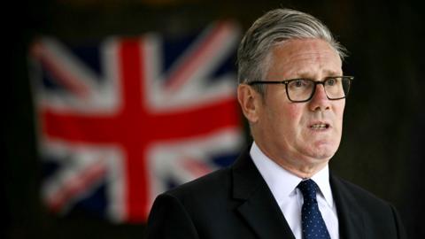 Sir Keir Starmer speaks while standing in front of a Union Jack flag.