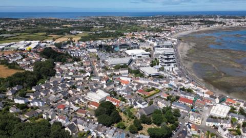 A drone photo taken above Guernsey. There is a number of properties and there is a beach to the right where the tide is out.