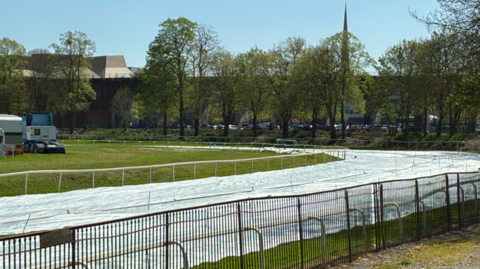Grey covers on the racecourse, going from the bottom left to about the middle right of the photo. Trees are in the background. 