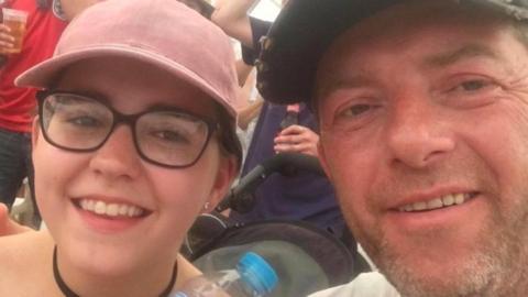 Bernadette Walker and Scott Walker are smiling at the camera in a selfie shot. She is wearing a pink baseball cap and he is also wearing a hat and has a stubbly beard