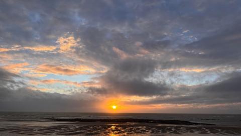 Grey sky over the coast with a setting sun in the distance 