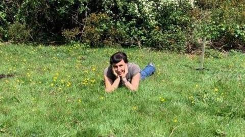 Sonia Rosenblatt lying on the grass at the nature reserve next to the trees that were planted