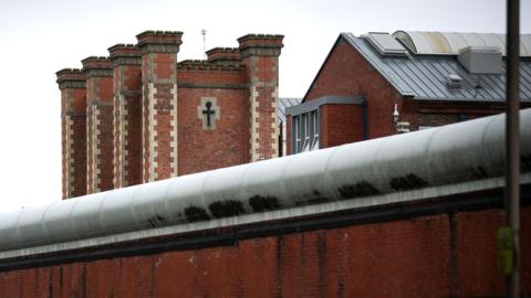 An exterior view of HM Prison Liverpool, an imposing red brick building seen behind a tall brick wall. 
