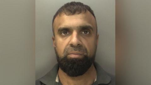 A close-up mug-shot of Yasir Khan with a grey background