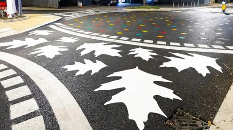 A pedestrian crossing painted with large leaves instead of standard white stripes