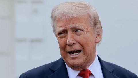 Donald Trump pictured in the middle of speaking, with his mouth open, dressed in a blue suit and red tie