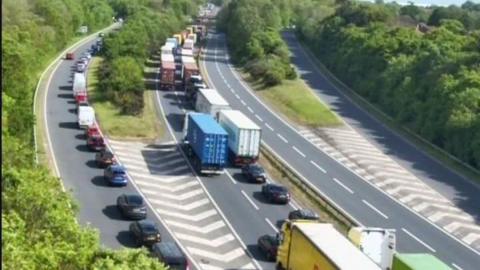 A traffic camera image from above of the A14 dual carriageway. There are long delays of vehicles. There is also a slip road that has been backed up with vehicles. 