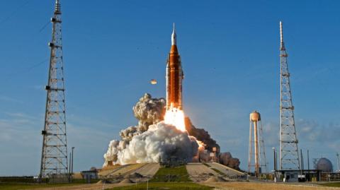 Rocket taking off with bright blue sky behind it.