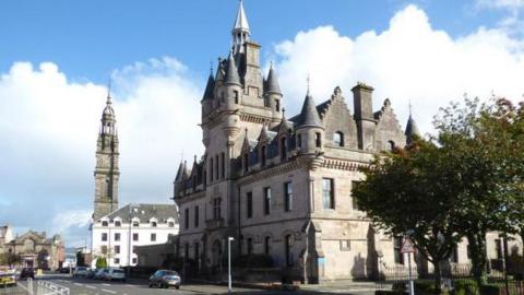 Old court building featuring a number of turrets and spires. There are other buildings on the same street, including a tower.