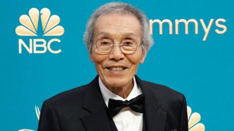 Picture of a smiling O Yeong Su wearing a black tuxedo standing in front of a blue background