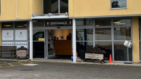 The entrance of the JSPCA Animal Shelter building. It has glass-fronted wall and automatic glass doors with a yellow first floor.