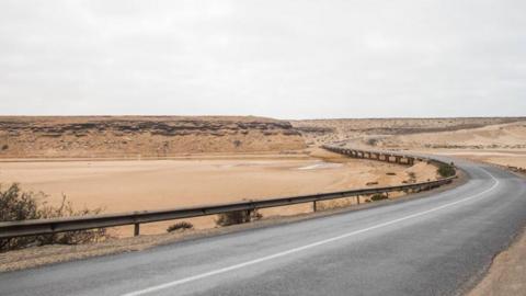a paved road cutting through a brown desert landscape